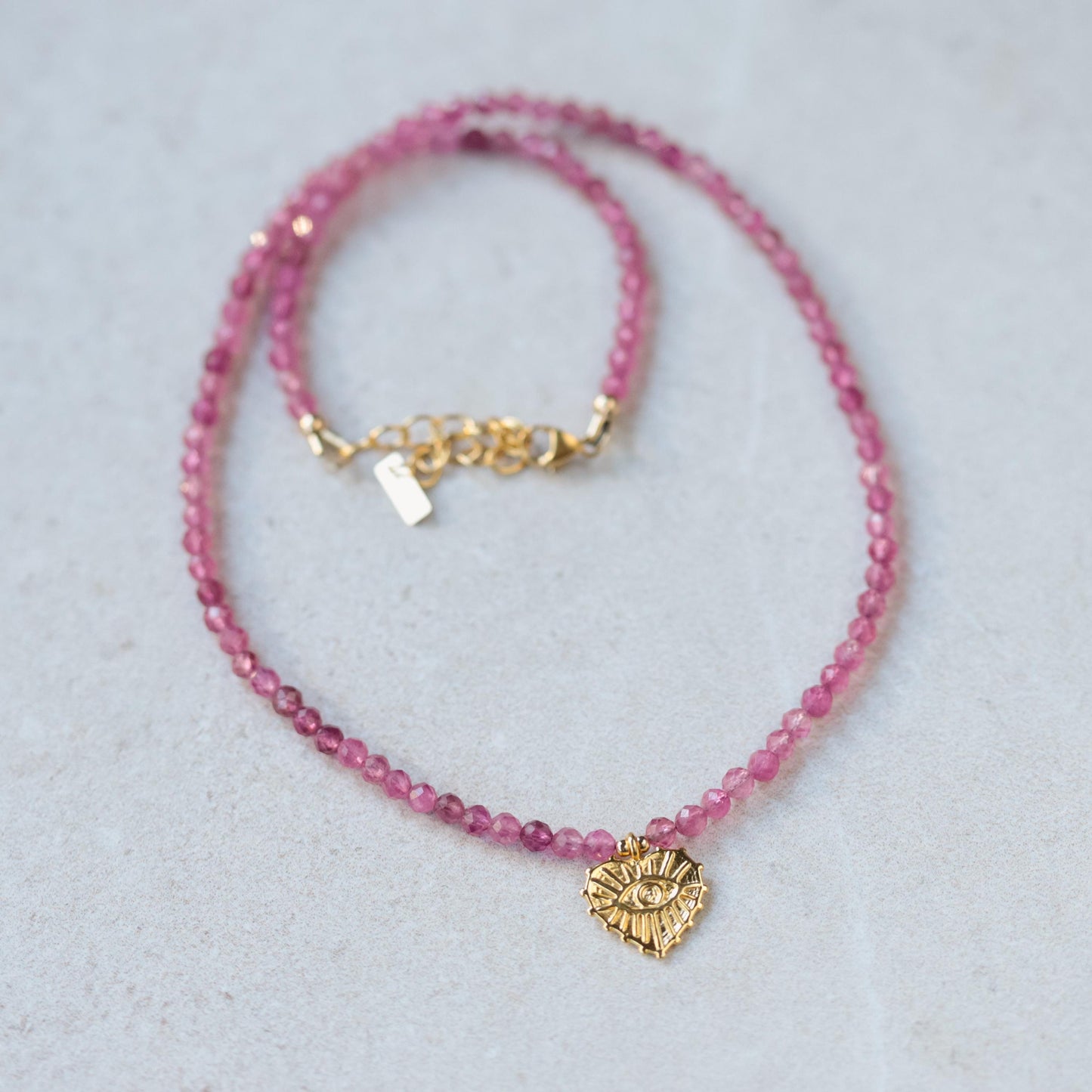 Pink tourmaline evil eye heart pendant from Earthly Abundance featuring a vibrant pink gemstone and protective evil eye design.