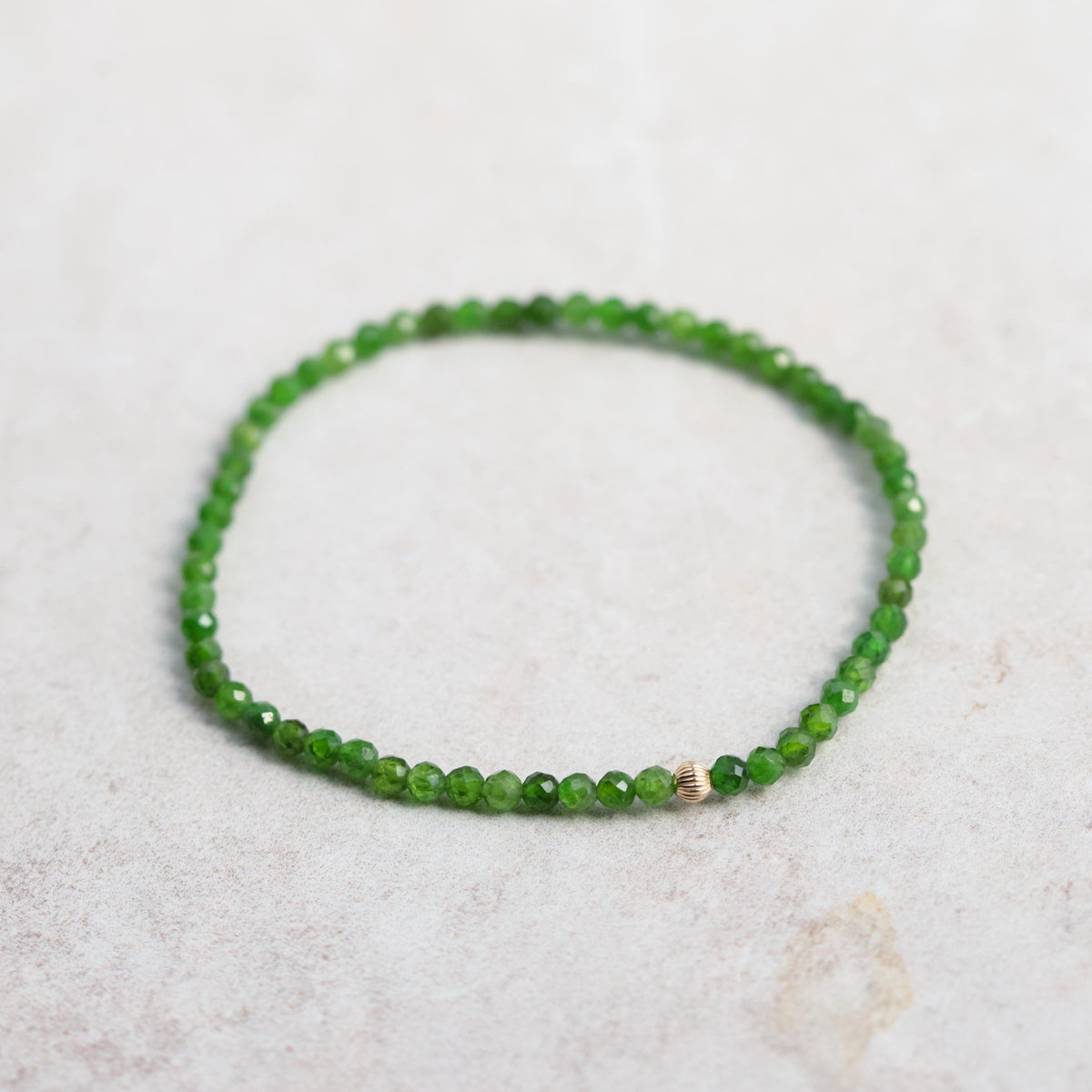 Shimmering chrome diopside gemstone set in a 14K gold jewelry piece, showcasing vibrant green color and intricate craftsmanship.