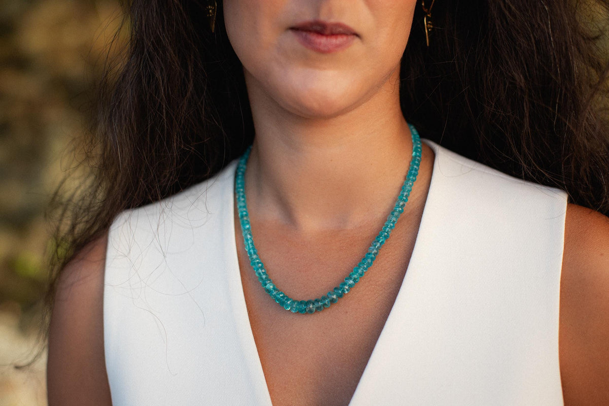 Glowing apatite necklace with vibrant blue-green gemstone pendant on a silver chain, displayed on a neutral background.