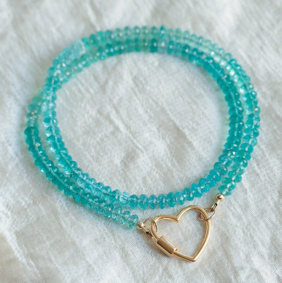 Aapatite heart pendant on a silver carabiner necklace from Earthly Abundance Jewelry, showcasing a blue-green gemstone heart.