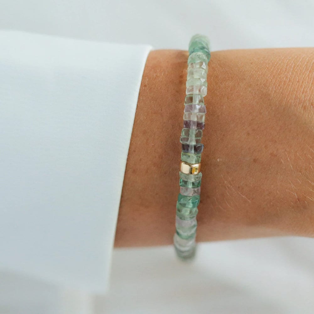 Earthly Abundance fluorite heishi bracelet with multicolored gemstone beads laid out in a row on a white background.