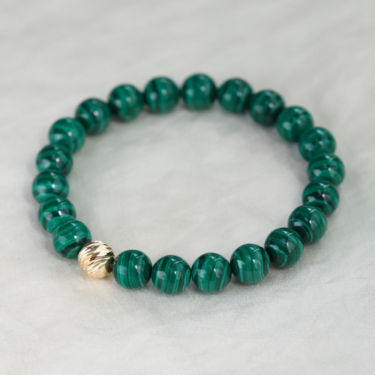 Round 8mm malachite gemstone beads from Earthly Abundance, showcasing vibrant green and natural banding on a jewelry strand.