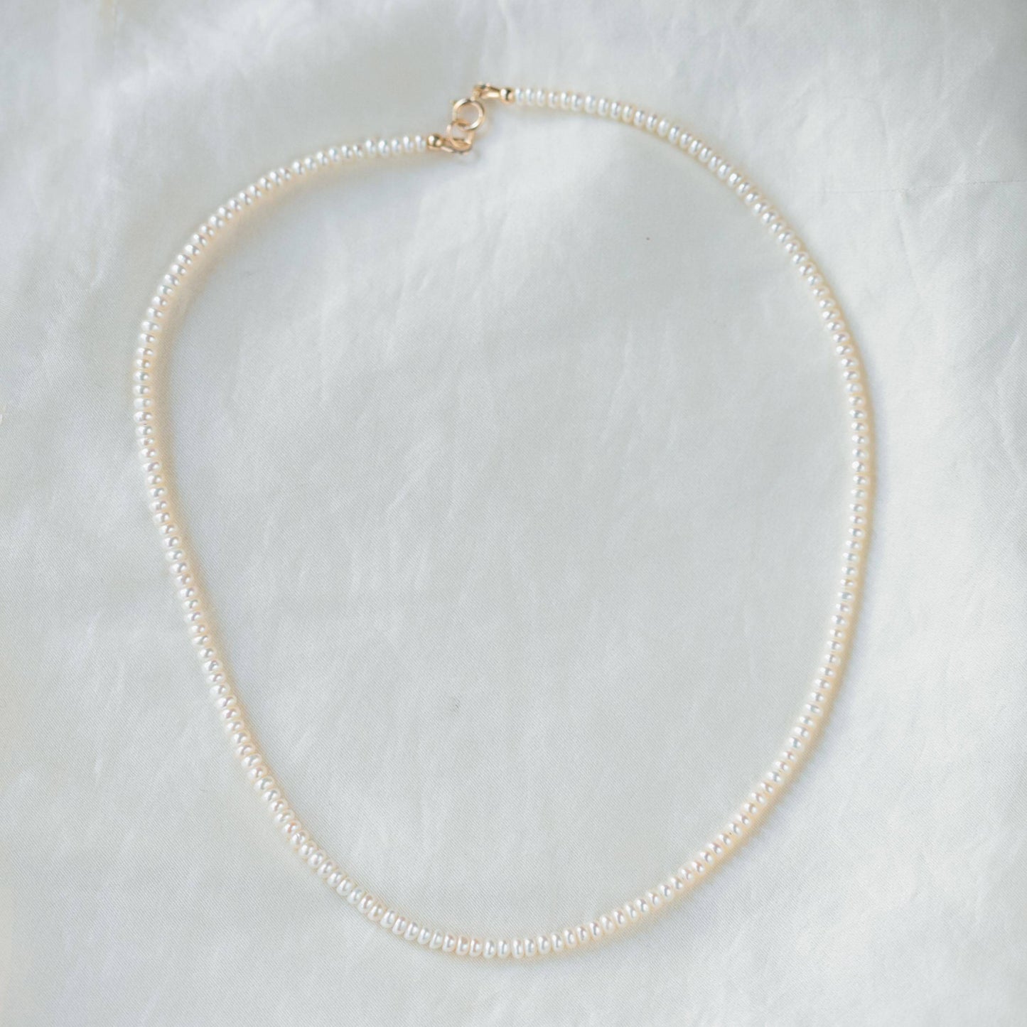 Freshwater pearl necklace with 14K gold clasp from Earthly Abundance Jewelry, showcasing lustrous white pearls on a delicate chain.