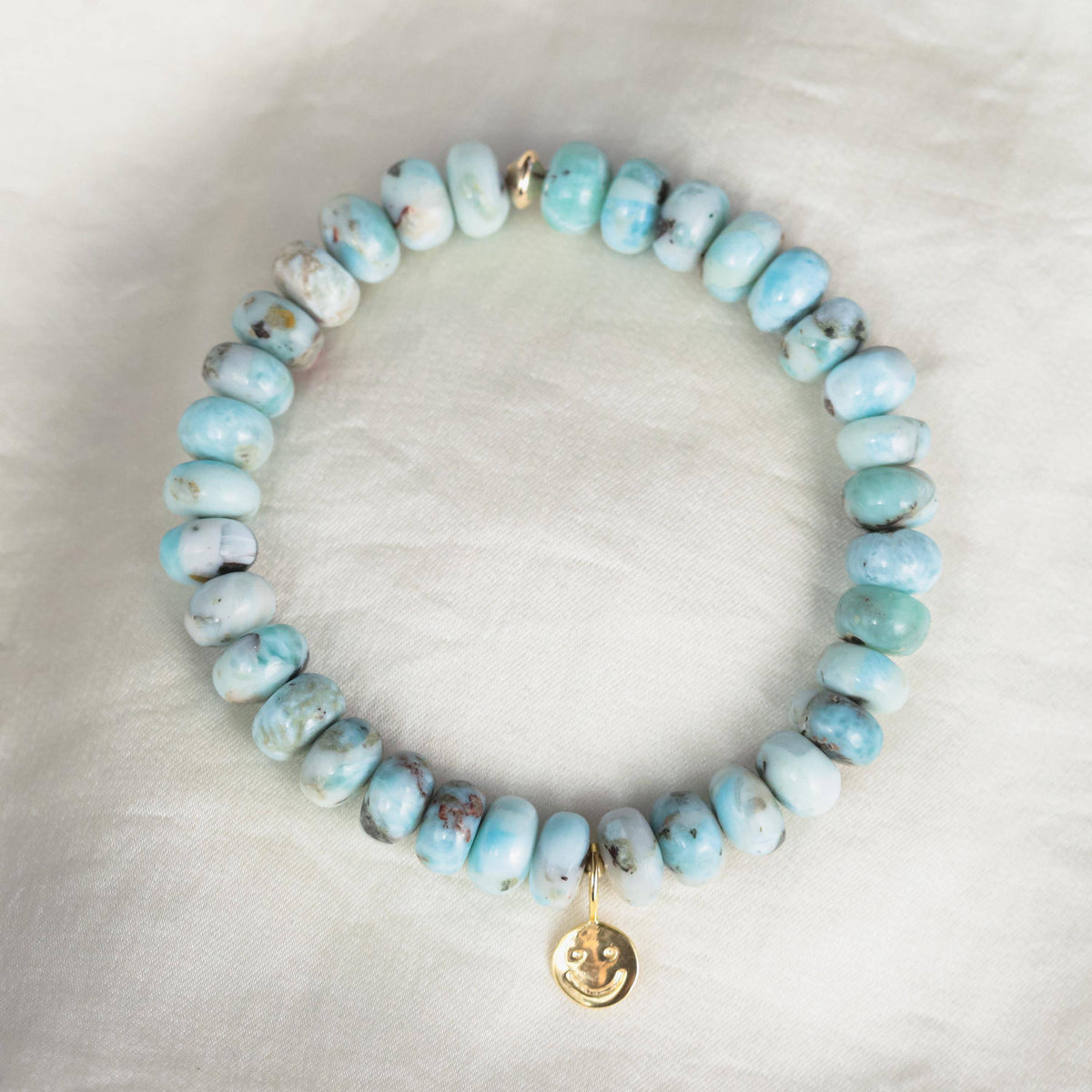 Larimar Smiley Bracelet by Earthly Abundance featuring round blue larimar beads and a smiling charm on a stretchy band.