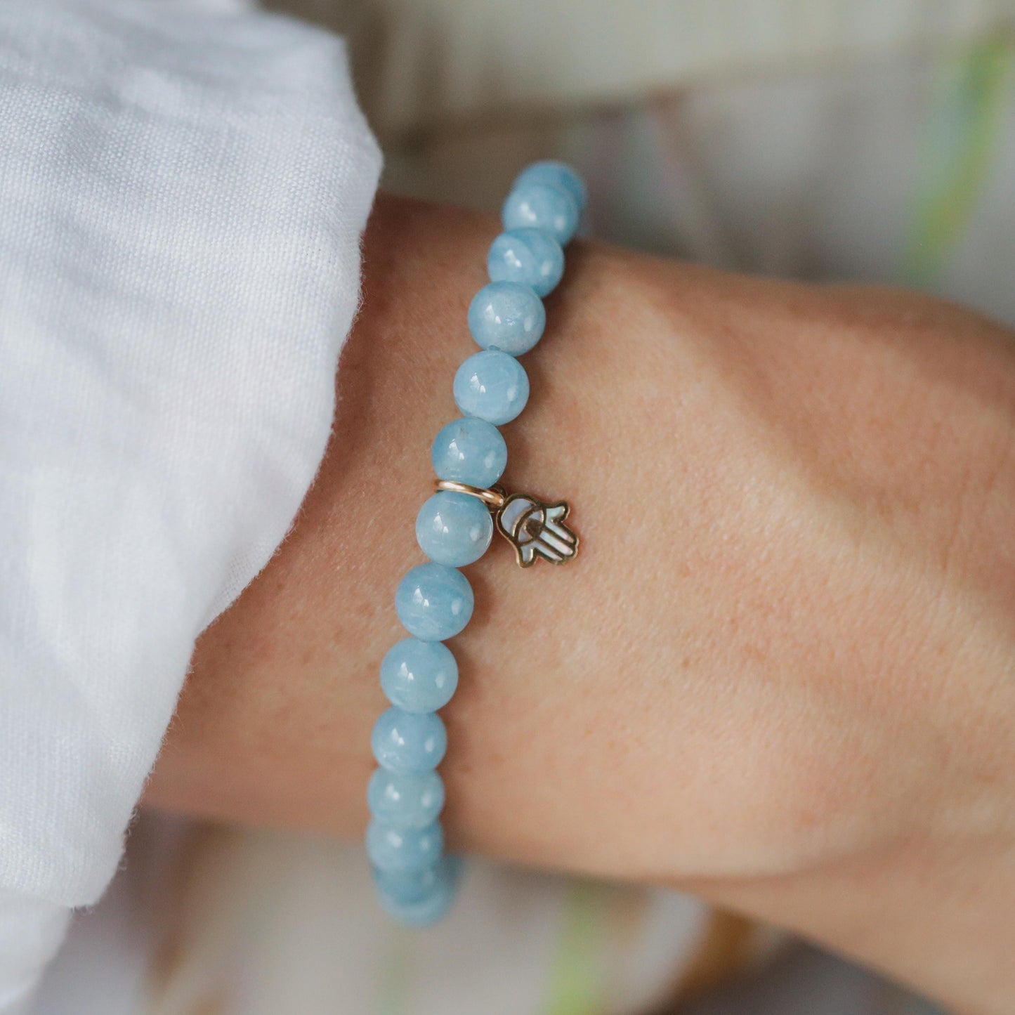 Aquamarine and mother of pearl Hamsa bracelet featuring intricate design and vibrant blue and iridescent accents.