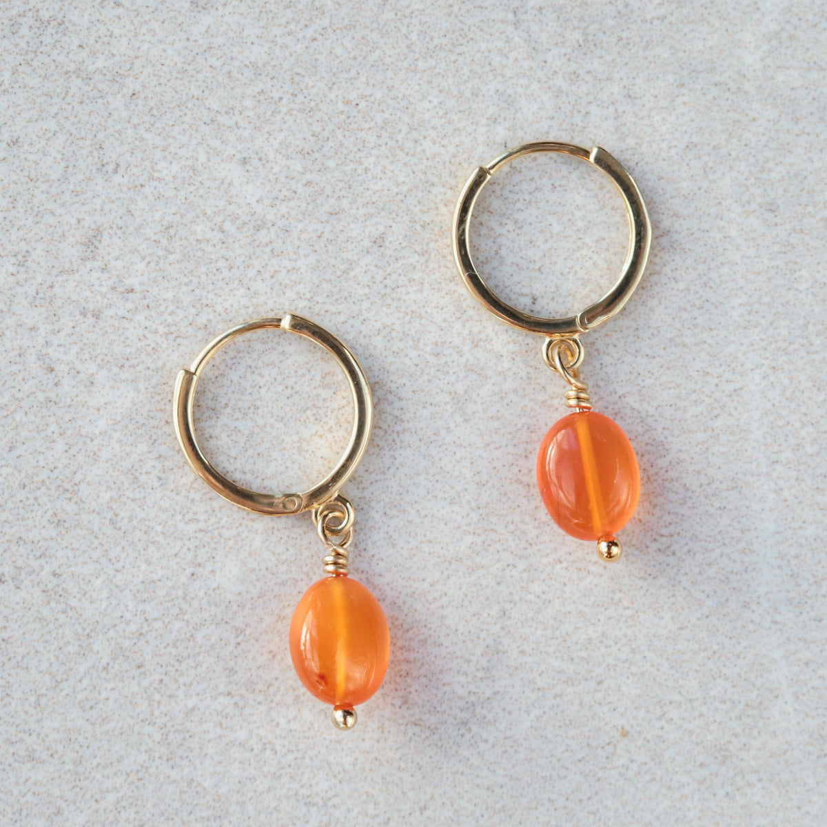 Earthly Abundance Carnelian glow hoops earrings featuring vibrant orange-red carnelian stones and gold-tone hoops.