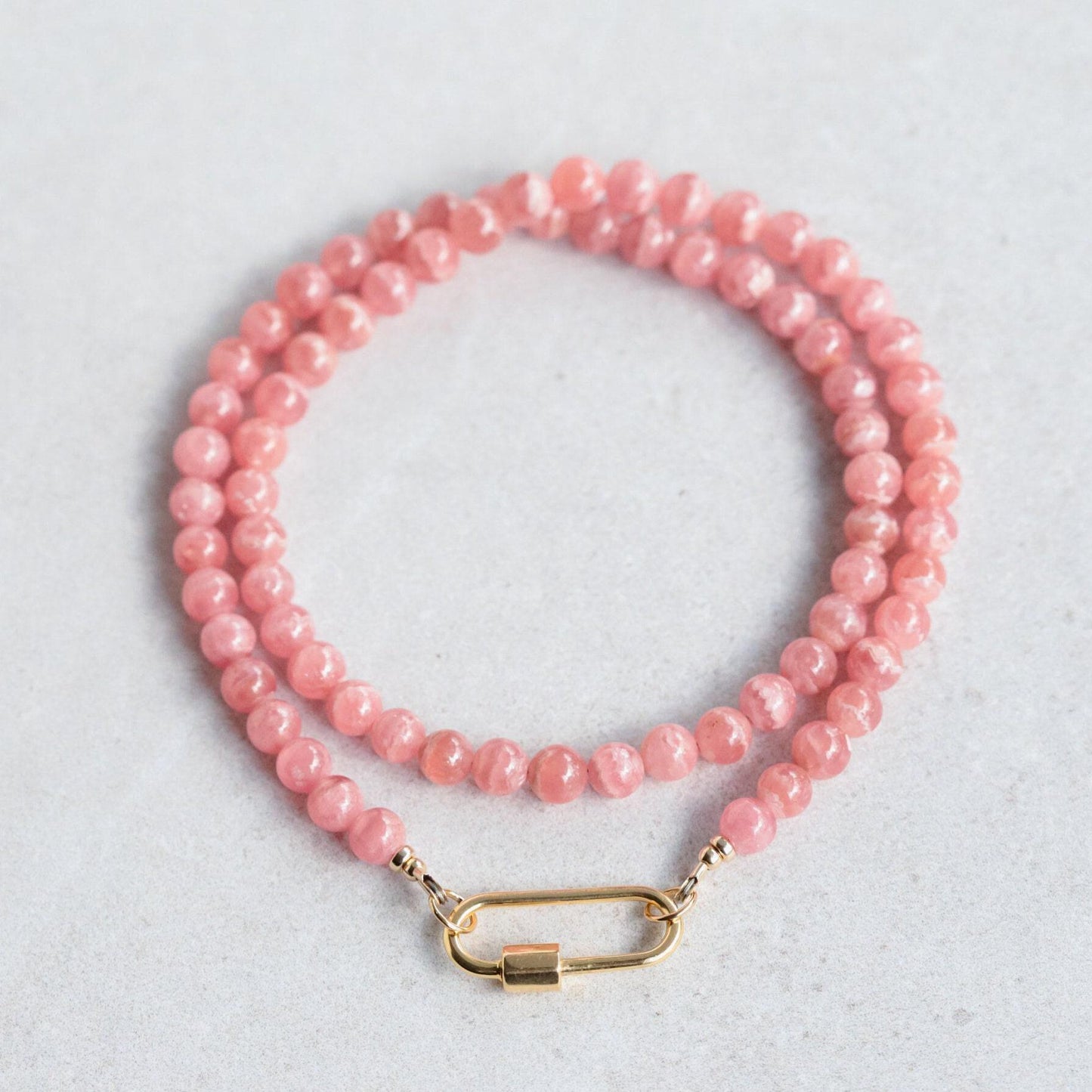 Earthly Abundance AAAA+ Rhodochrosite carabiner necklace with polished pink gemstone and silver-tone clasp, close-up view.