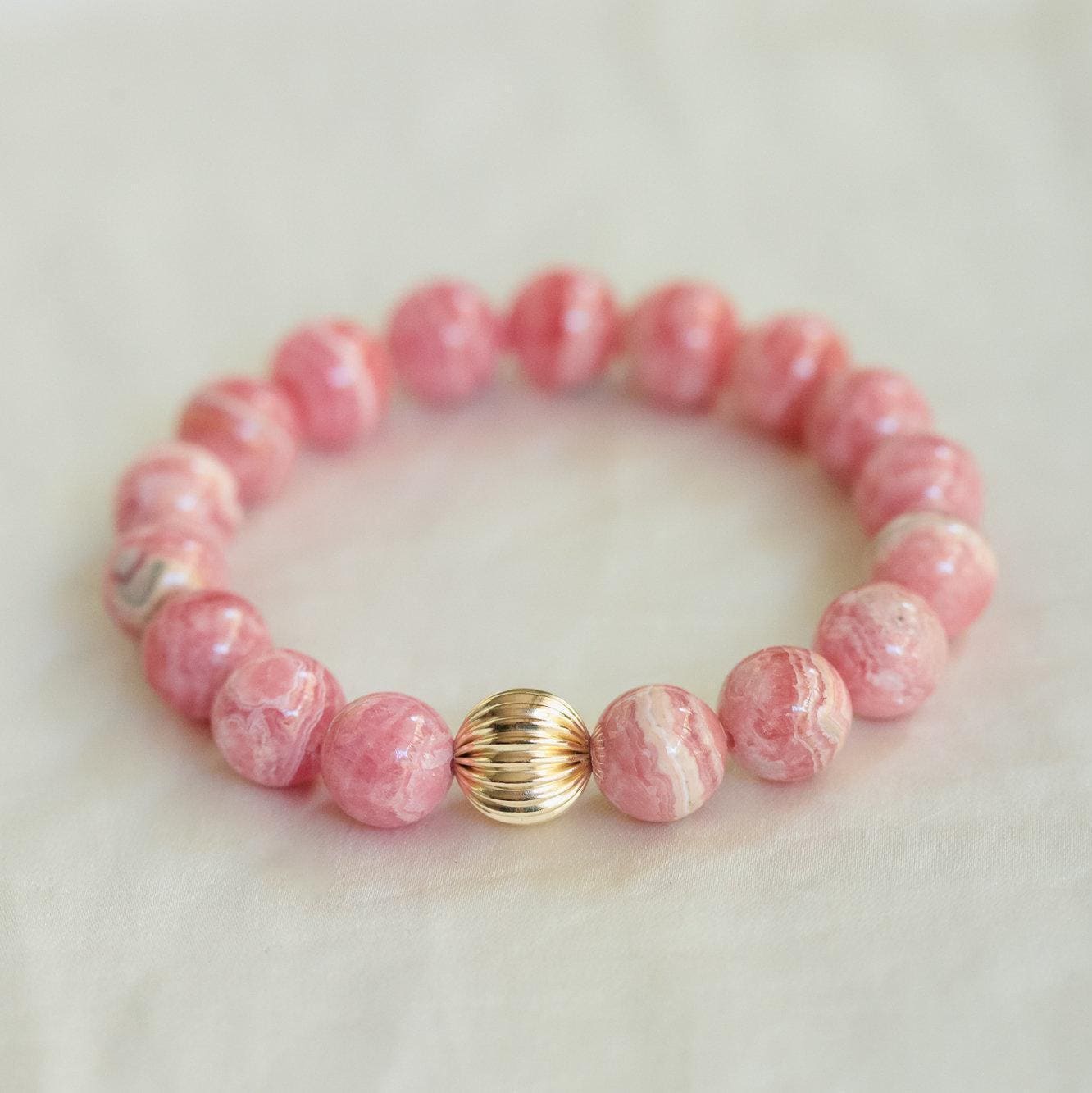 Smooth 10mm Rhodochrosite gemstone bead from Earthly Abundance, showcasing vibrant pink and red hues with natural stone texture.