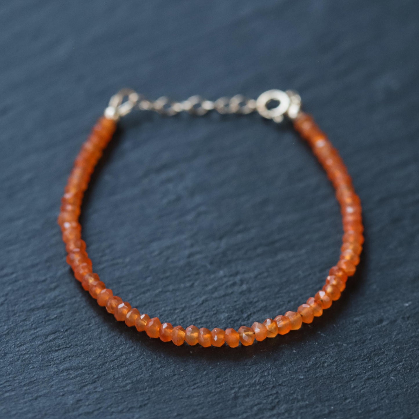 Carnelian bracelet with 14K gold accents, featuring polished orange gemstones, styled on a delicate gold chain.