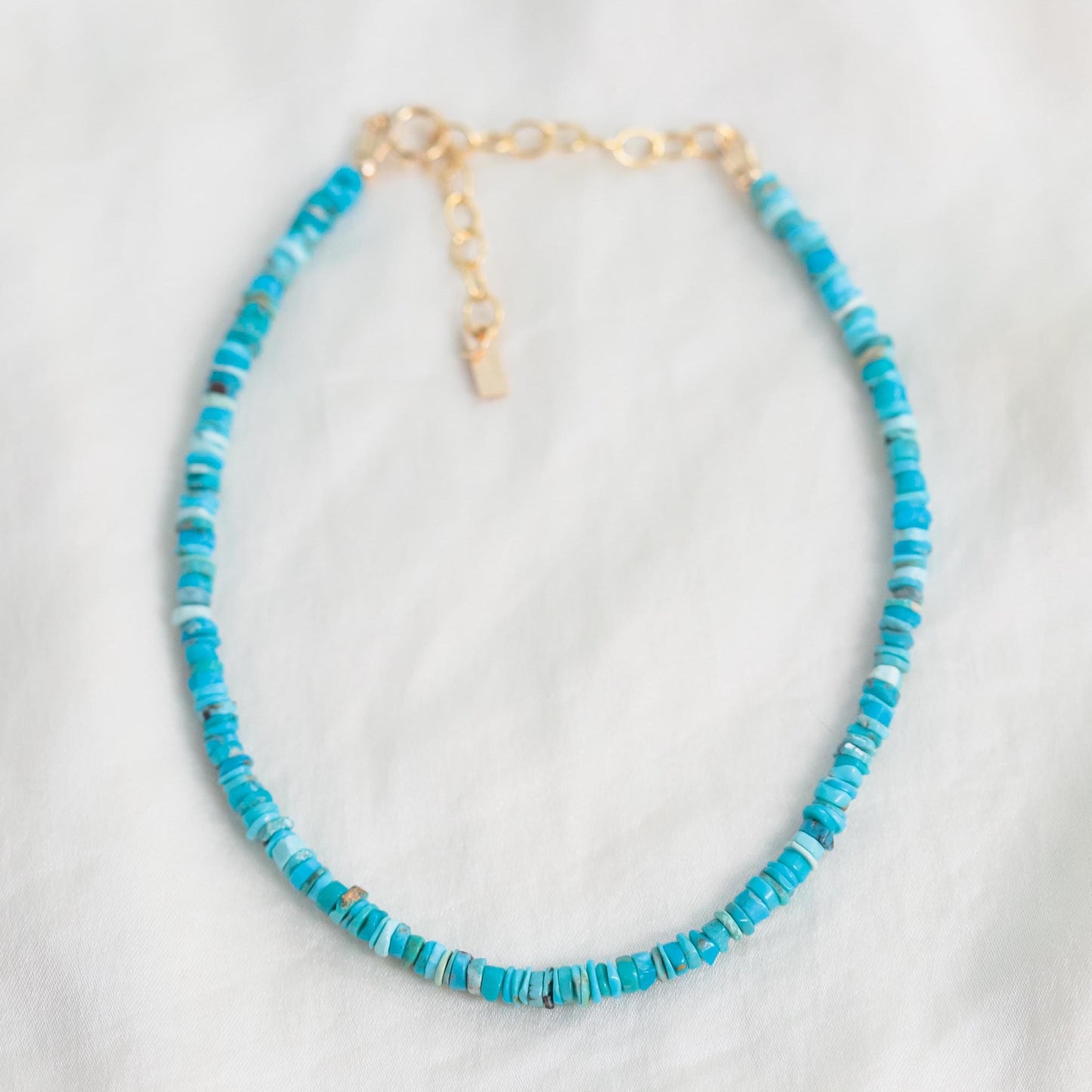 Earthy Abundance turquoise heishi anklet with textured beads and earthy tones, worn on an ankle in a natural setting.