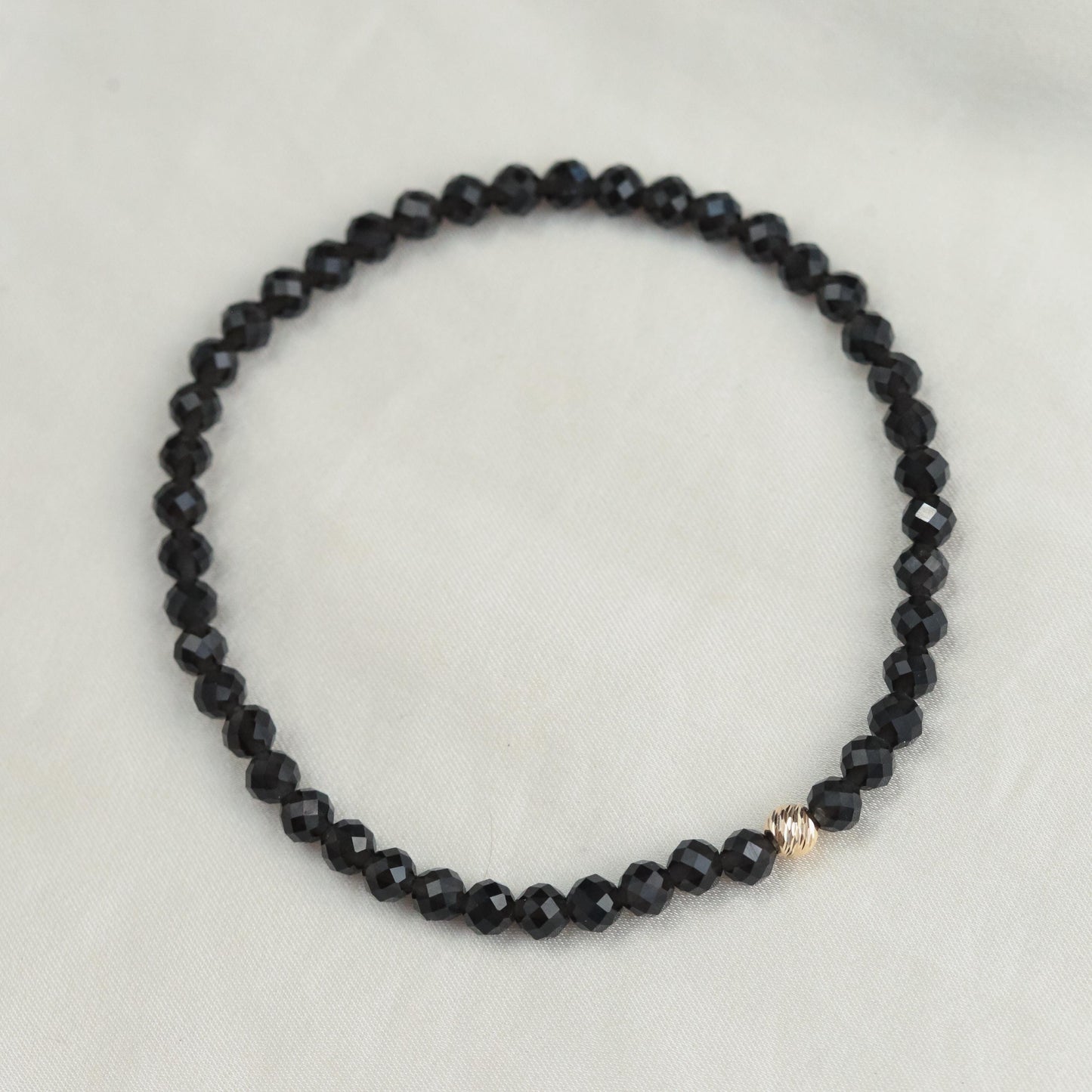 Black Obsidian bracelet with 4mm beads from Earthly Abundance, featuring a close-up of the polished stone beads arranged in a circle.