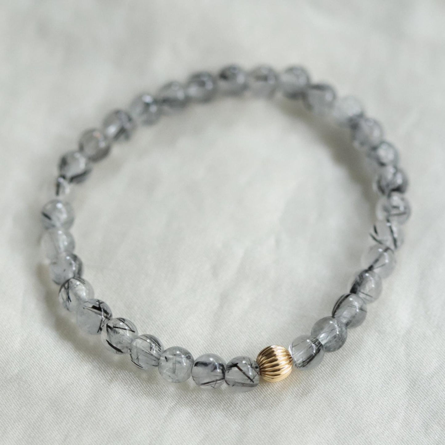 Black rutilated quartz gemstone from Earthly Abundance Jewelry showing dark needle-like inclusions and polished surface.
