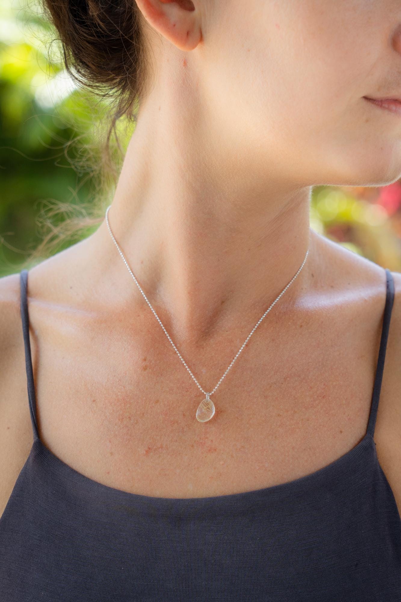Rutilated Quartz pendant necklace from Earthly Abundance featuring a polished gemstone with golden needle inclusions on a silver chain.