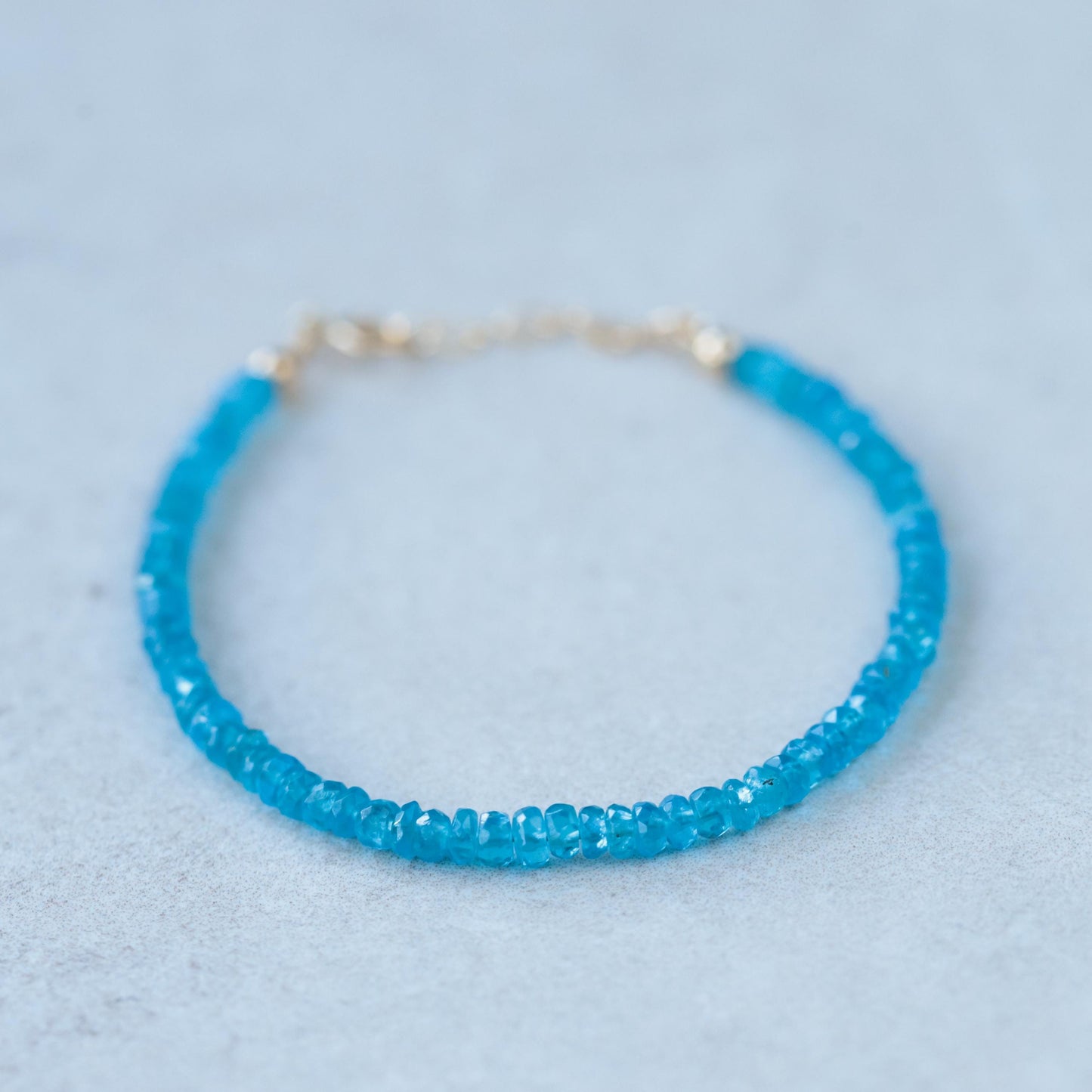 Apatite bracelet with 14K gold clasp, featuring vibrant blue-green apatite gemstones, on a neutral background.