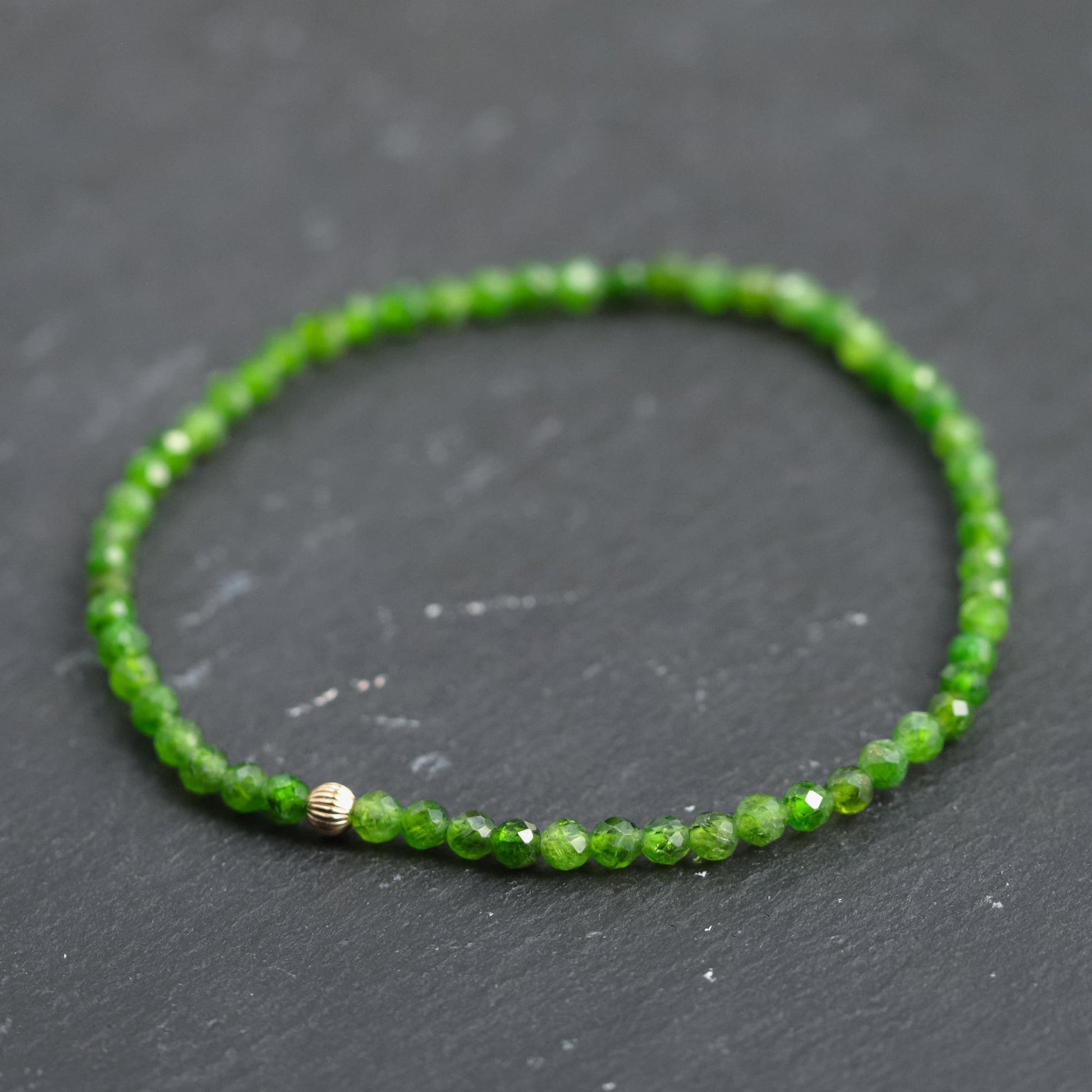 Shimmering chrome diopside gemstone set in a 14K gold setting, showcasing vibrant green hues and polished surface.