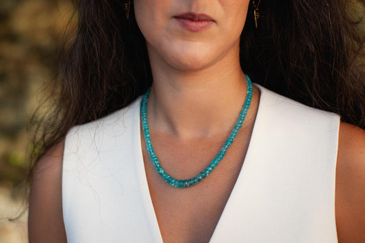 Glowing apatite necklace with vibrant blue-green gemstone pendant on a silver chain, displayed on a neutral background.