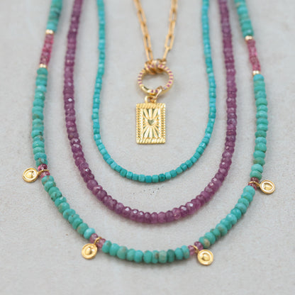 African Ruby necklace featuring vibrant red gemstones on a delicate gold chain, styled with elegant jewelry.