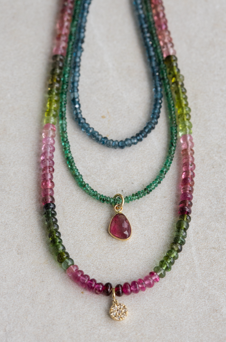 Layered blue, green, and pink gemstone necklaces with gold pendants