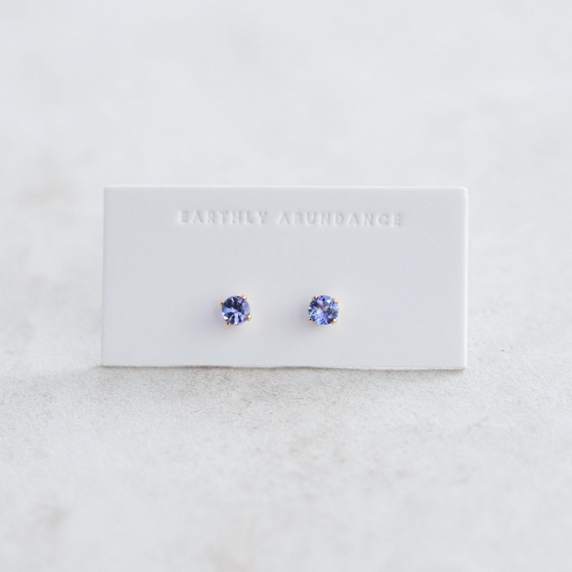Pair of Tanzanite stud earrings with silver settings, showcasing vibrant blue-purple gemstones on a white background.