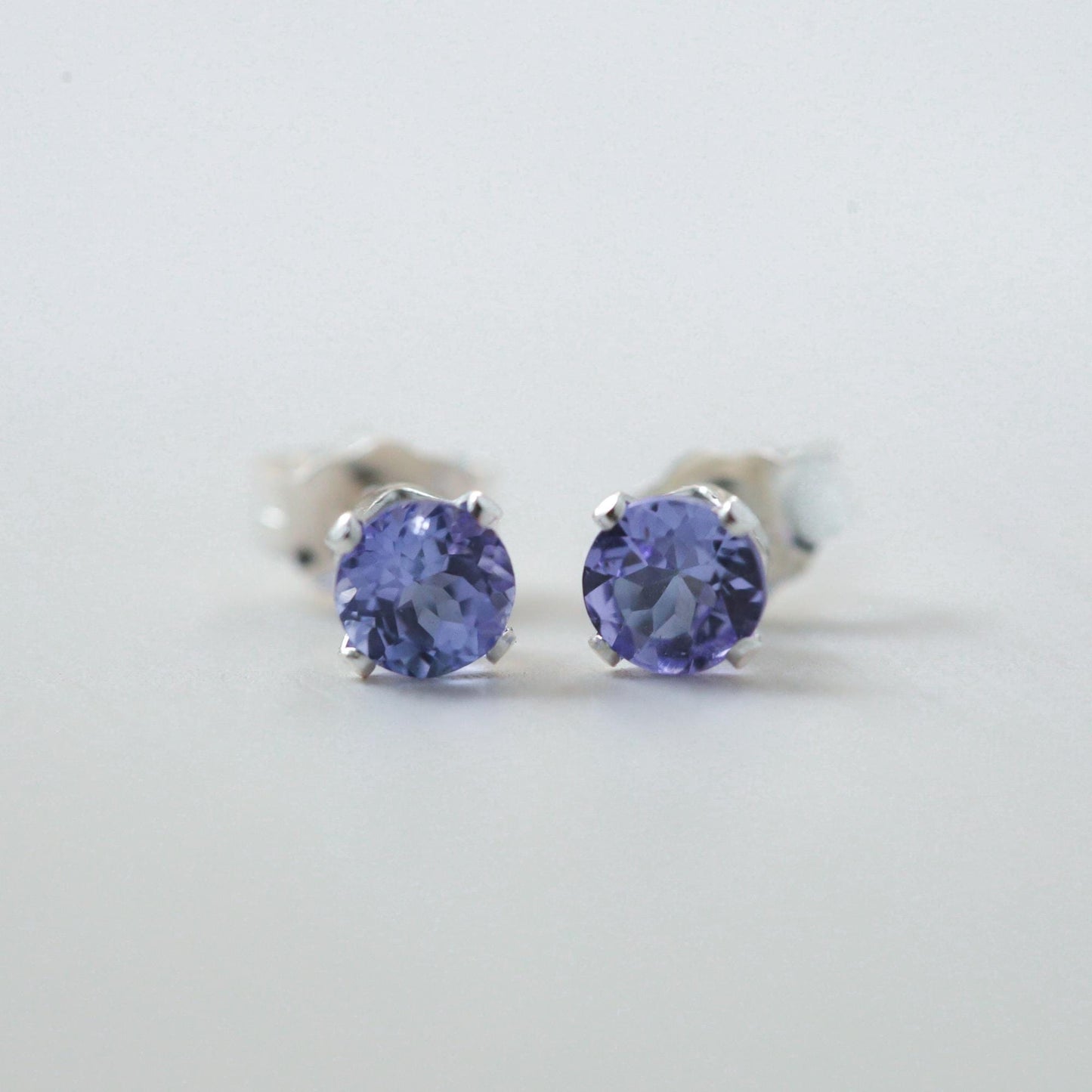 Earthly Abundance tanzanite stud earrings with oval-cut purple gemstones and silver stud settings, close-up view of the jewelry.