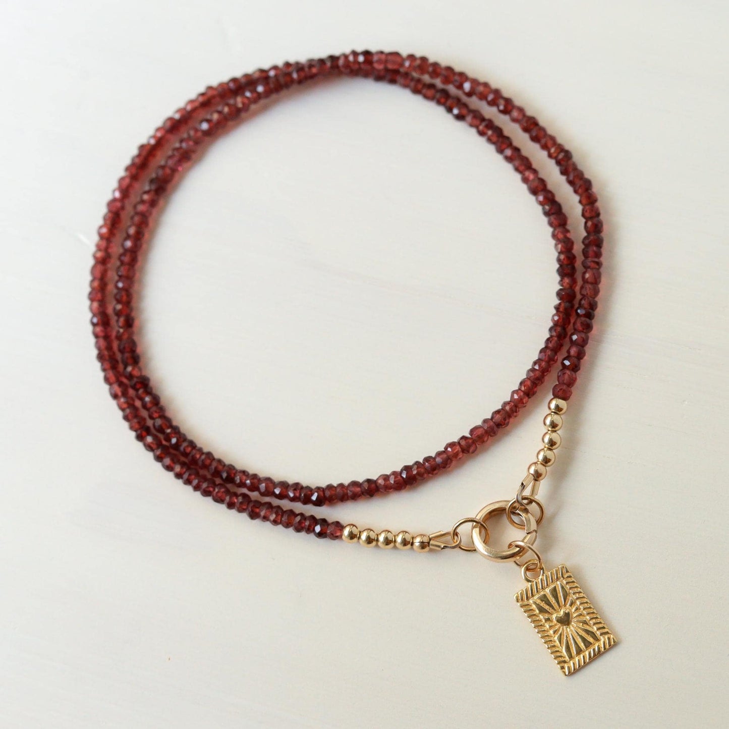 Earthly Abundance Amor Garnet Necklace featuring a polished garnet gemstone pendant on a delicate chain.