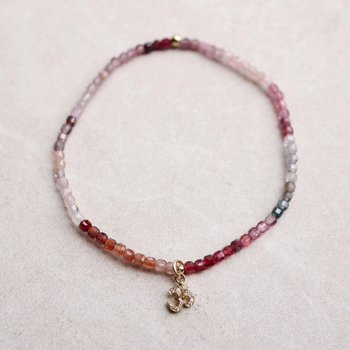 Multicolor spinel and diamond om bracelet in solid 14K gold, featuring vibrant gemstones and intricate design.